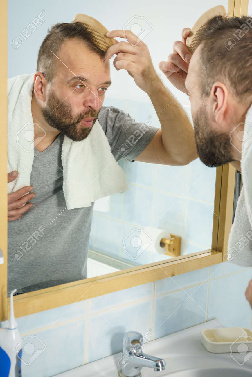 Adult Man Standing In Front Of The Bathroom Mirror Brushing His