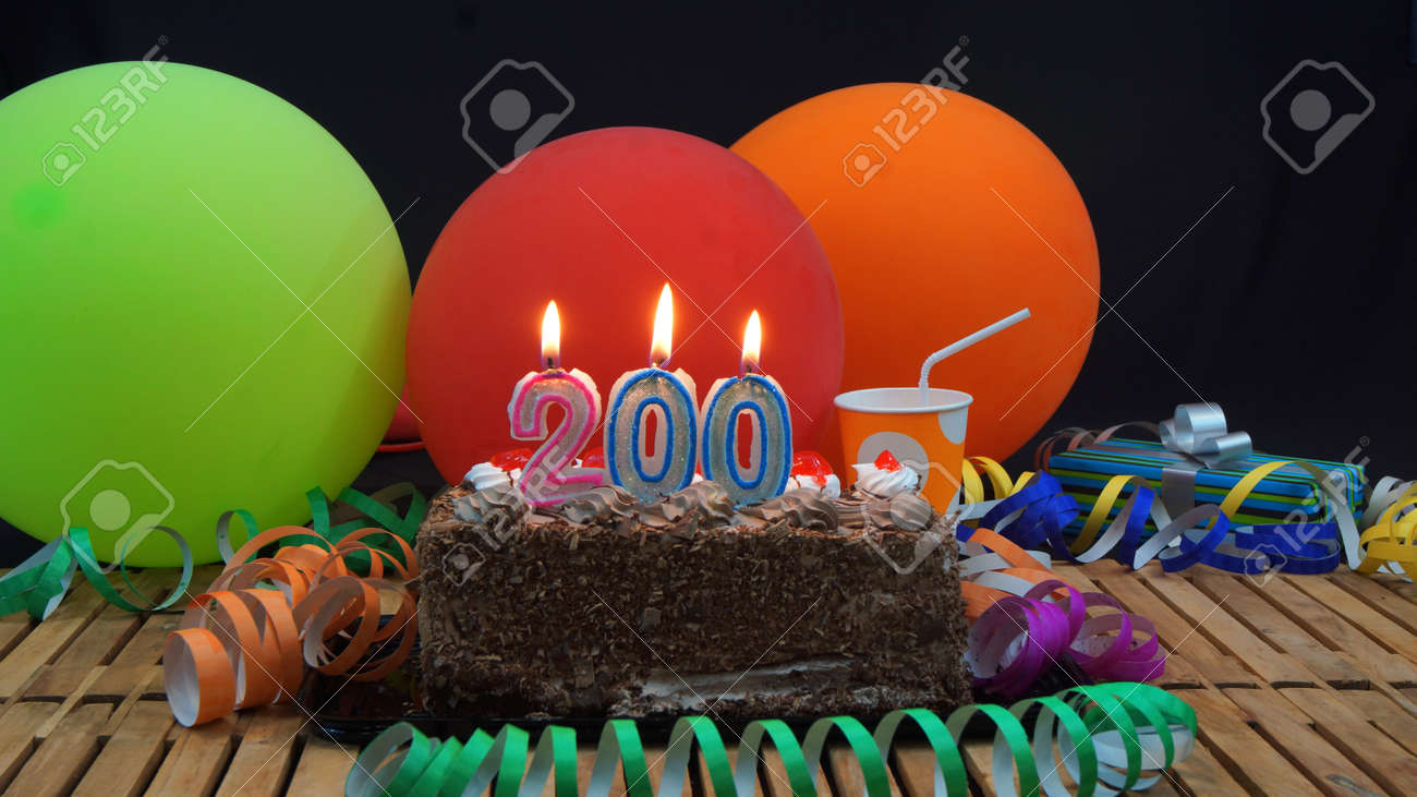 Chocolate birthday cake with candles burning on rustic wooden table with background of colorful balloons, gifts, plastic cups and streamers with black background - 68820939 Chocolate birthday cake with candles burning on rustic wooden table with background of colorful balloons, gifts, plastic cups and streamers with black background - 68820939