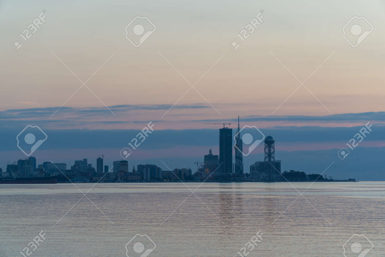 Batumi At Sunset. View From Sea Beach To Cityscape With Modern Urban Architecture Skyscraper. Georgia. - 77010379 Batumi At Sunset. View From Sea Beach To Cityscape With Modern Urban Architecture Skyscraper. Georgia. - 77010379