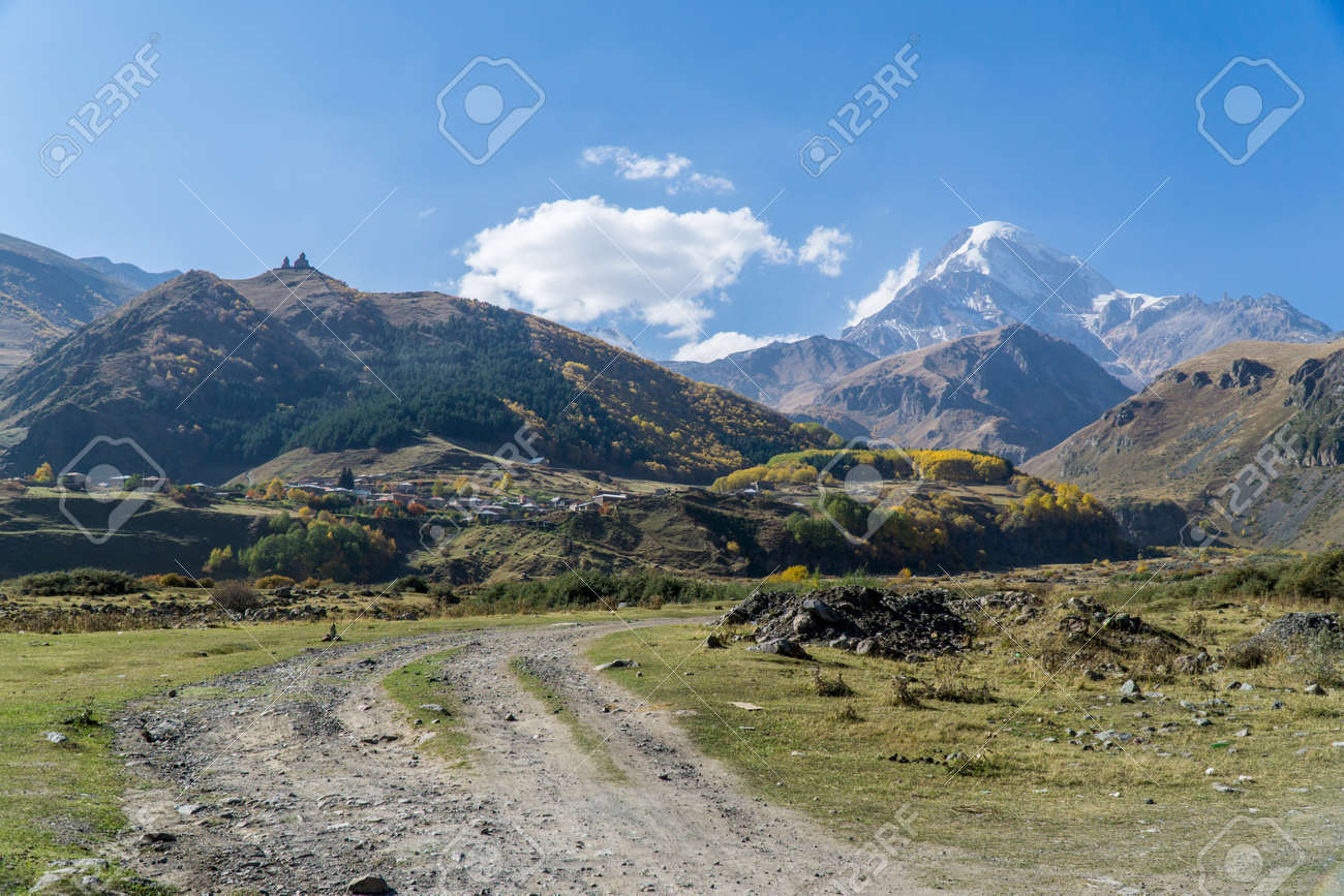 View of village Stepantsminda, Gergeti Trinity Church and mount Kazbek in Sunny weather - 77008092 View of village Stepantsminda, Gergeti Trinity Church and mount Kazbek in Sunny weather - 77008092