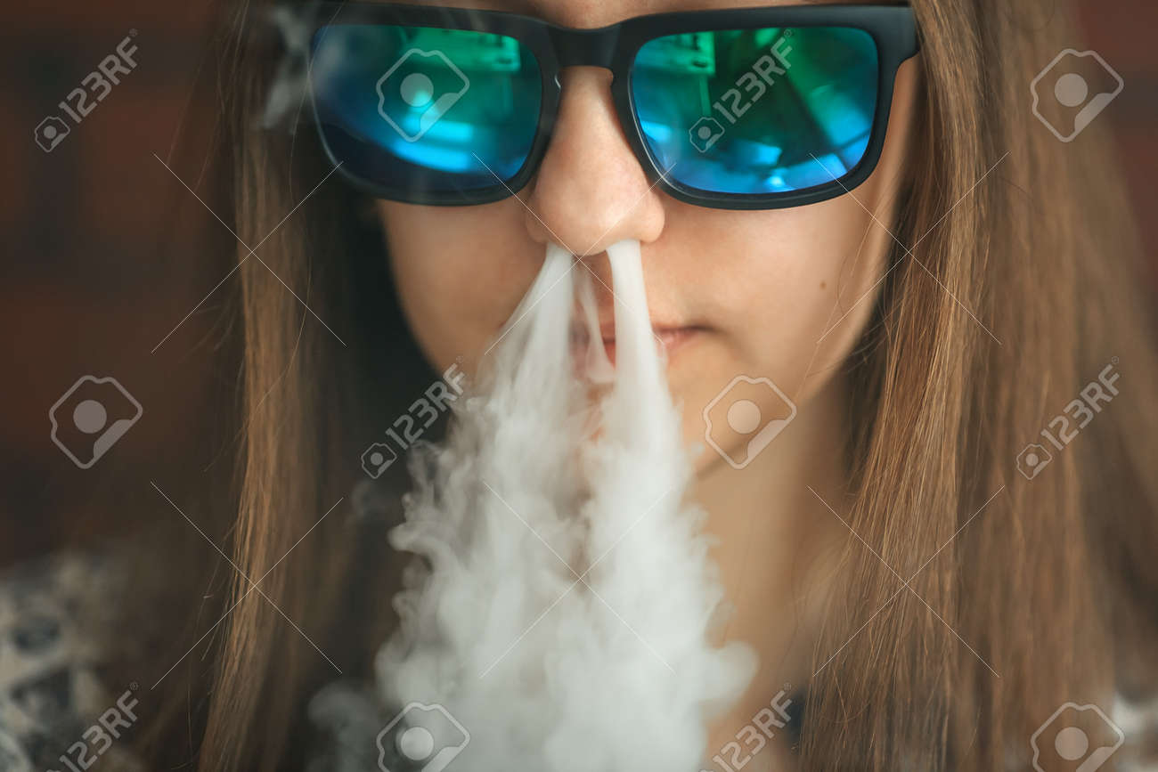 Vape. Jeune fille blanche belle dans des lunettes de soleil admet des bouffées de vapeur de la cigarette électronique. Vaping. Adolescent. Vape. Jeune fille blanche belle dans des lunettes de soleil admet des bouffées de vapeur de la cigarette électronique. Vaping. Adolescent.