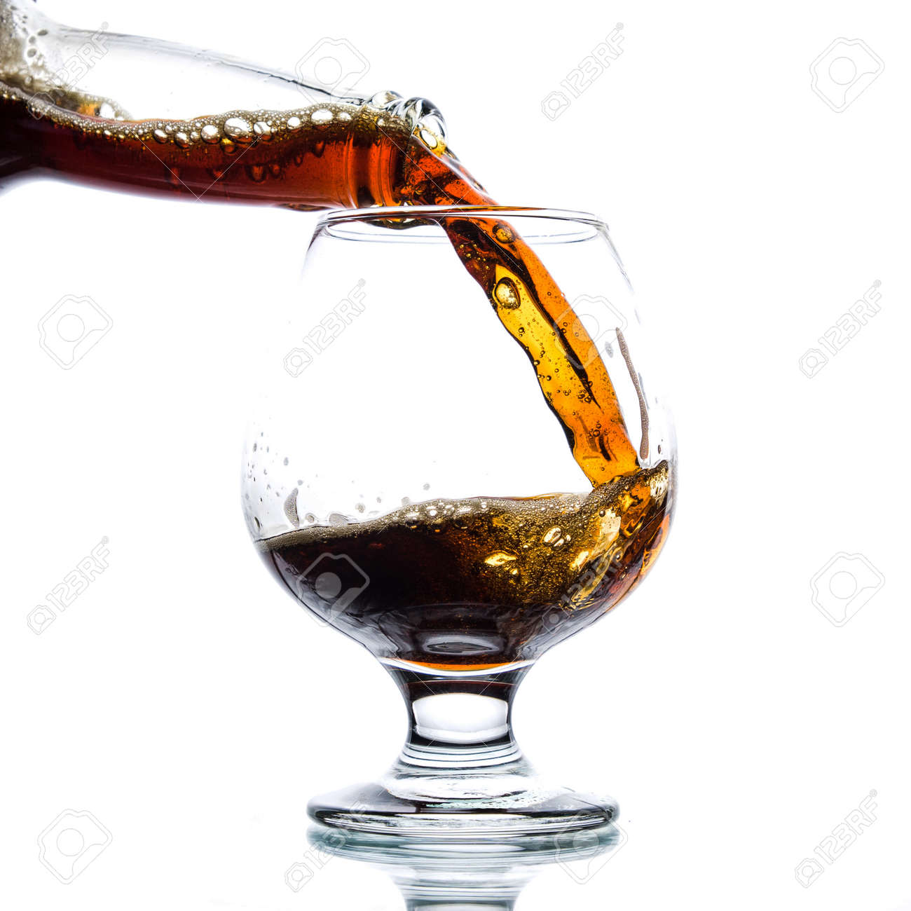 Brown ale pours from a bottle into a glass on a light background - 152811670 Brown ale pours from a bottle into a glass on a light background - 152811670