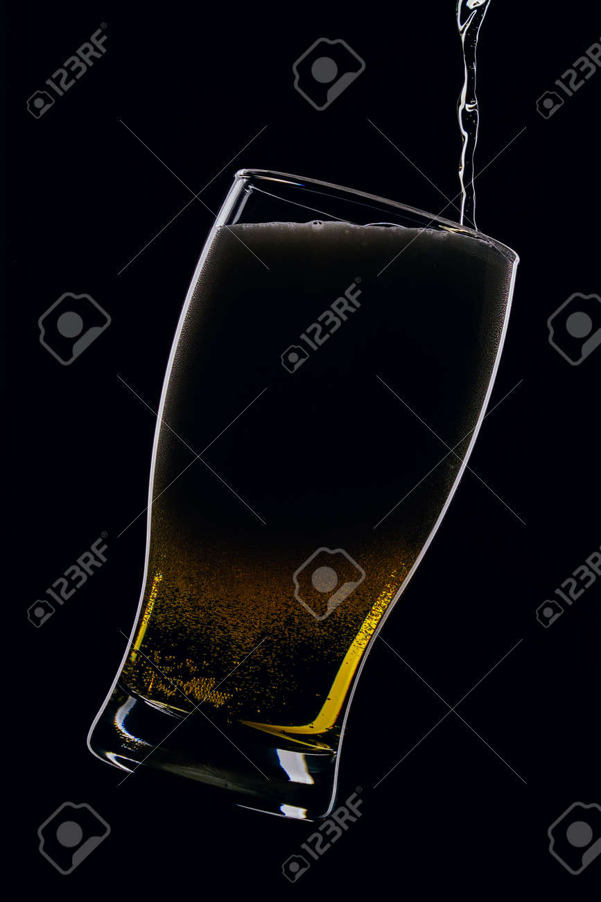 Lager beer pours from a bottle into a glass on a black background - 152811748 Lager beer pours from a bottle into a glass on a black background - 152811748