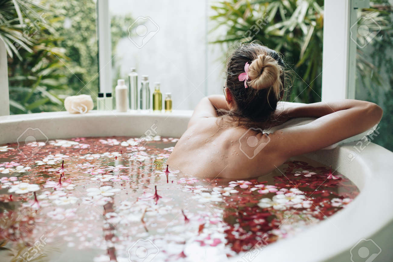 woman relaxing in round outdoor bath with tropical flowers, organic