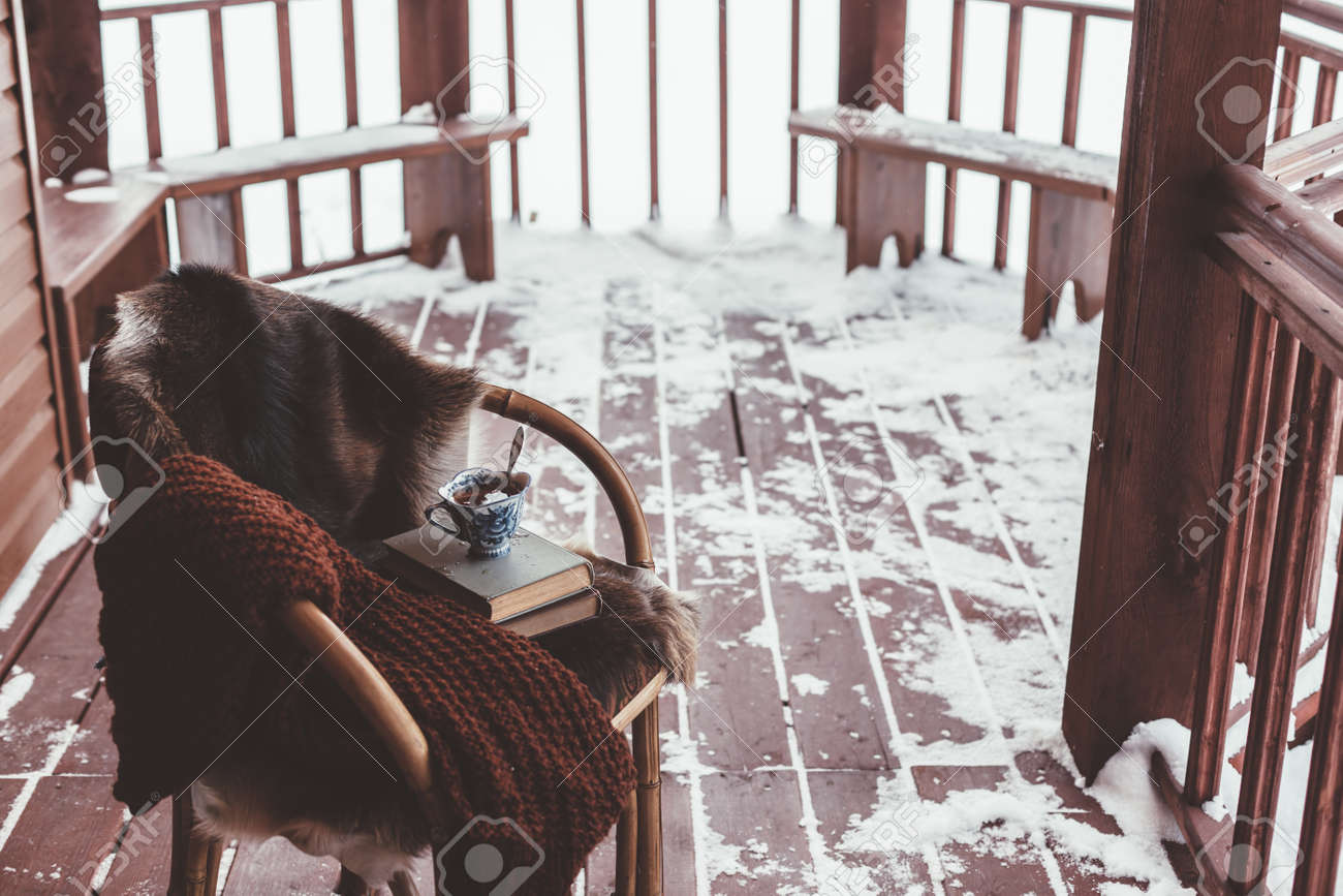 雪で丸太小屋のベランダ デッキに毛皮の椅子 お茶 暖かい毛布 読書 寒い冬の週末のリラックス の写真素材 画像素材 Image