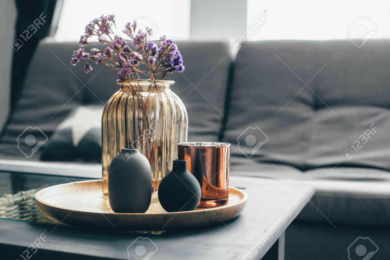 Home interior decor in gray and brown colors: glass jar with dried flowers, vase and candle on the wooden tray on the coffee table over sofa. Living room decoration. - 85971656 Home interior decor in gray and brown colors: glass jar with dried flowers, vase and candle on the wooden tray on the coffee table over sofa. Living room decoration. - 85971656