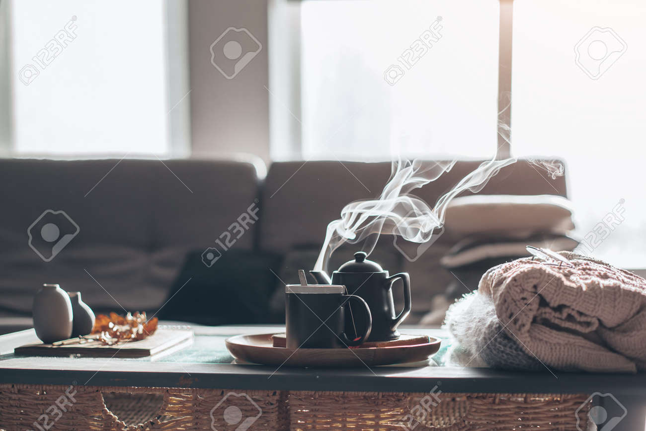 Still life details in home interior of living room. Sweaters and cup of tea with steam on a serving tray on a coffee table. Breakfast over sofa in morning sunlight. Cozy autumn or winter concept. - 85981994 Still life details in home interior of living room. Sweaters and cup of tea with steam on a serving tray on a coffee table. Breakfast over sofa in morning sunlight. Cozy autumn or winter concept. - 85981994
