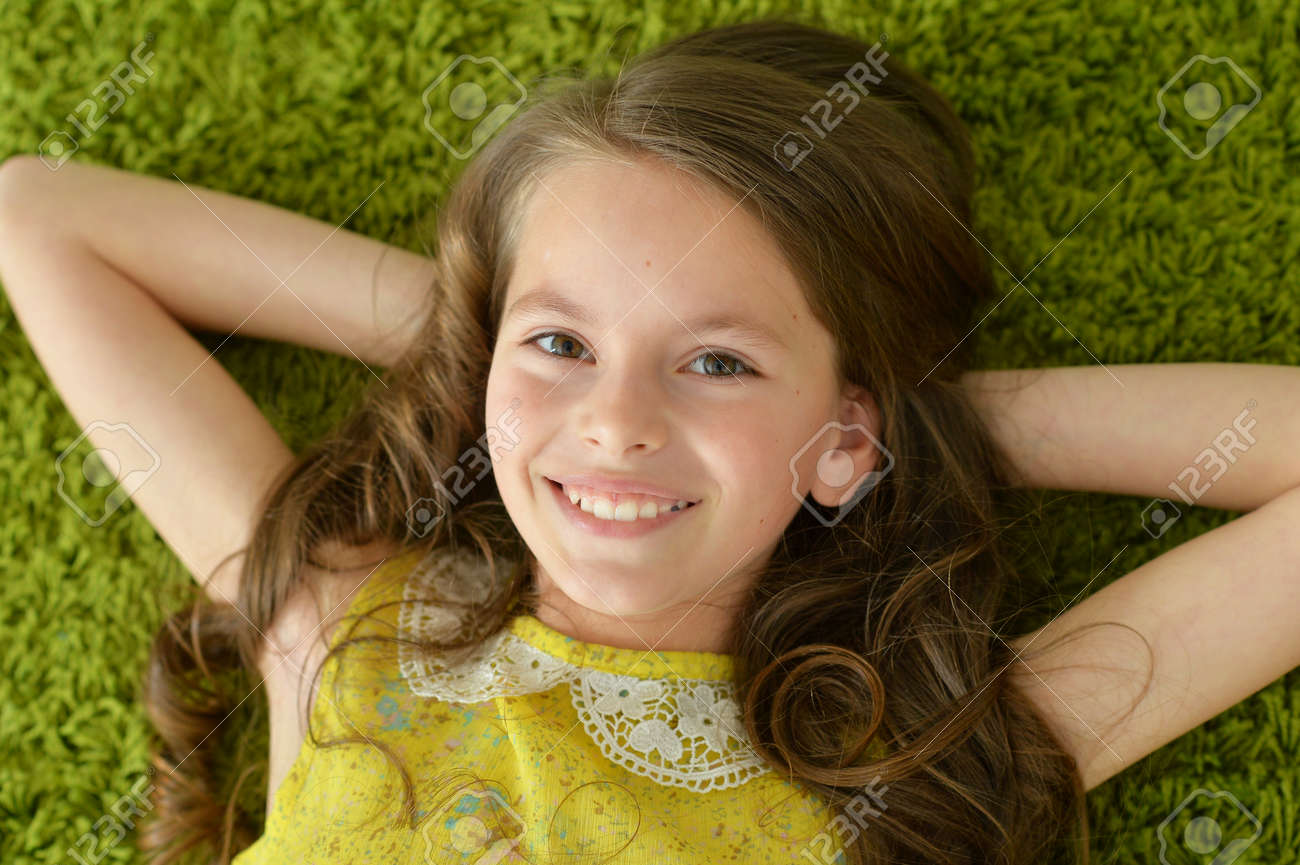 Close-up portrait of funny smiling little girl lying on green carpet - 114614564 Close-up portrait of funny smiling little girl lying on green carpet - 114614564