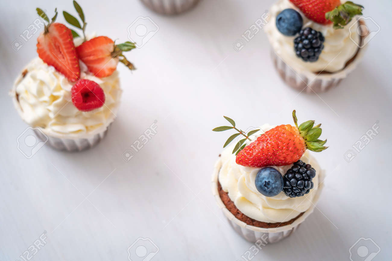 Fresh and delicious cupcakes with yogurt cream and fresh berries. Cakes with cream, strawberries, blueberries, blackberries and raspberries are on table in kitchen. Muffin with cream. Close up - 145936931 Fresh and delicious cupcakes with yogurt cream and fresh berries. Cakes with cream, strawberries, blueberries, blackberries and raspberries are on table in kitchen. Muffin with cream. Close up - 145936931