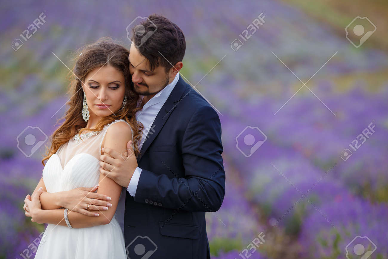 夏の日の結婚式新郎新婦の愛の若いカップル ラベンダー畑で愛と幸福の瞬間をお楽しみください 背景の明るい青空に豪華なウェディング ドレスの花嫁 の写真素材 画像素材 Image