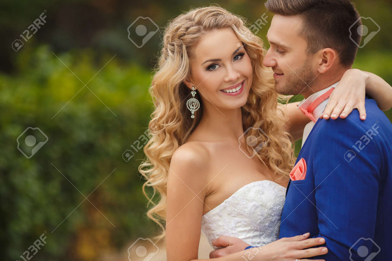 夏緑自然の野外を歩いている日を結婚式で新郎新婦ブライダルのカップル 幸せな新婚女と男を受け入れ 緑豊かな公園でキスします 屋外の結婚式のカップルを愛しています 新郎新婦 の写真素材 画像素材 Image