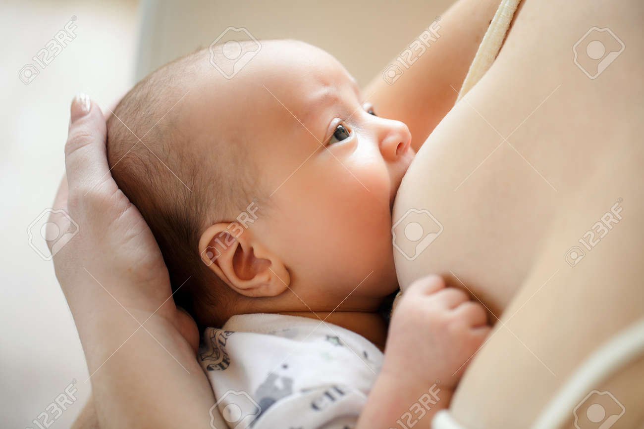 若い女性は 白のナイトガウンを着てください 彼女少し茶色の目の息子を保持している胸をしゃぶり静かには シャツの画像と白いの周り探している慎重に服を着てください の写真素材 画像素材 Image