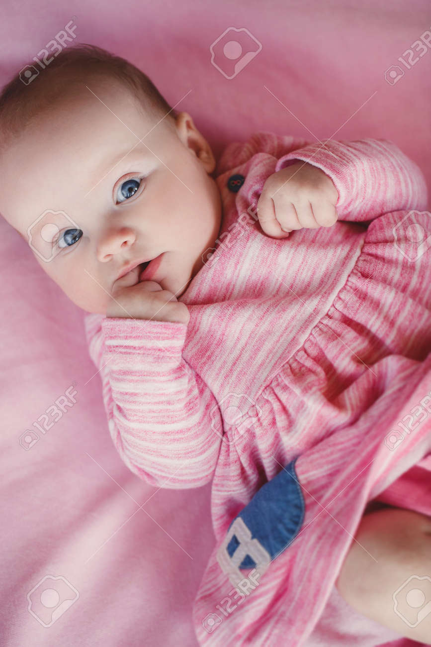 Little Baby Girl With Short Hair And Blue Eyes Wearing A Pink