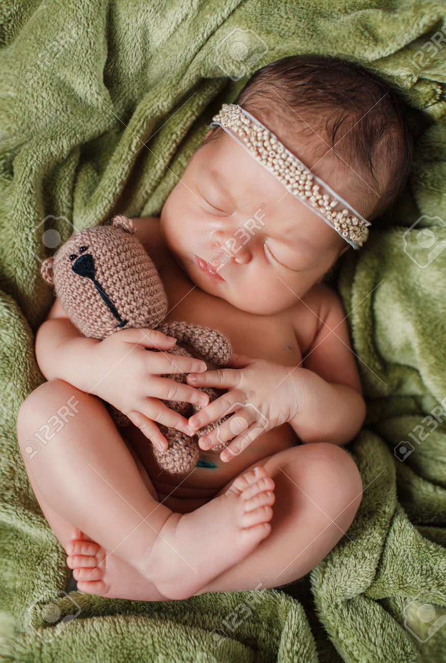 彼の頭に花輪をかぶったかわいい子供 動物のぬいぐるみを抱いて緑のベッドの上の生まれたばかりの赤ちゃんの安らかな眠り甘く眠っている茶色のクマのぬいぐるみを抱いて緑の毛布に腕や足に隠れています の写真素材 画像素材 Image