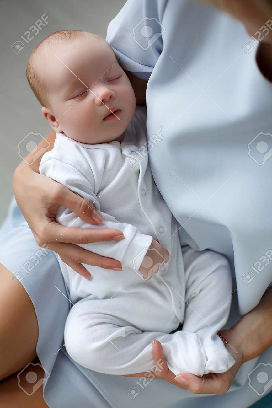 Portrait D Un Bebe Nouveau Ne Dormir Avec Un Peu De Cheveux Blonds Vetus De Combinaisons Blanches Bebe Qui Dort Dans Les Bras De La Mere Assise Mere Vetue D Une Robe Blanche Tient Le