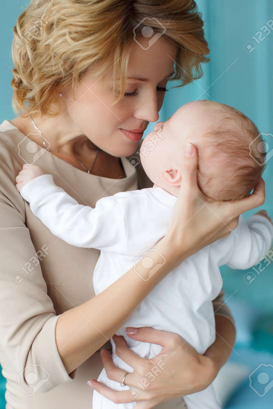 Jeune Femme Belle Avec Des Cheveux Blonds Epais Vetue D Une Robe De Couleur Beige Porte Autour De Son Cou Une Chaine En Argent Avec Un Pendentif Tenant Son Fils Nouveau Ne Le Bebe