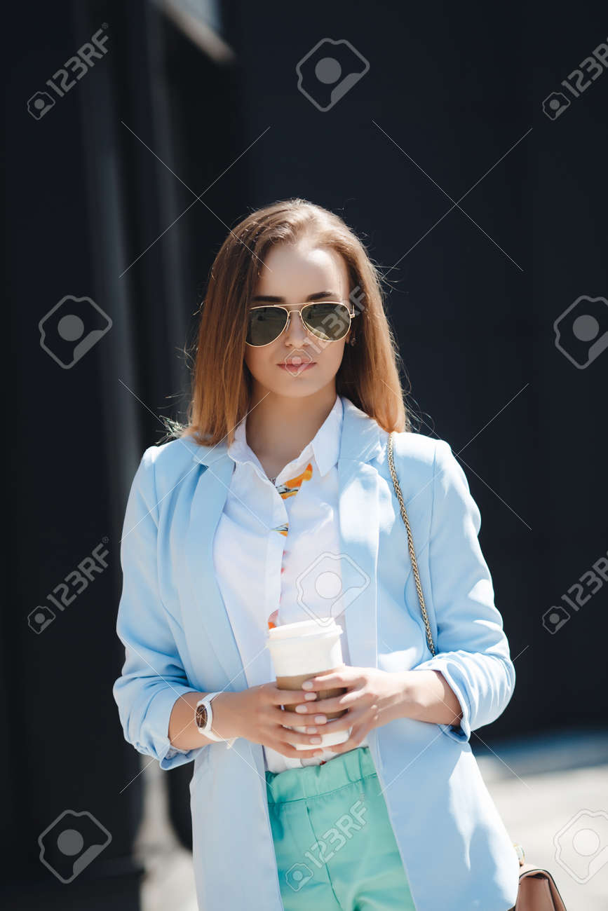 Une Femme Elegante Jeune Et Belle Avec Un Pantalon Bleu Une Chemise Blanche Un Sac A Main En Beige Des Cheveux Longs Et Legers Des Maquillage Leger Des Lunettes De Soleil Posant