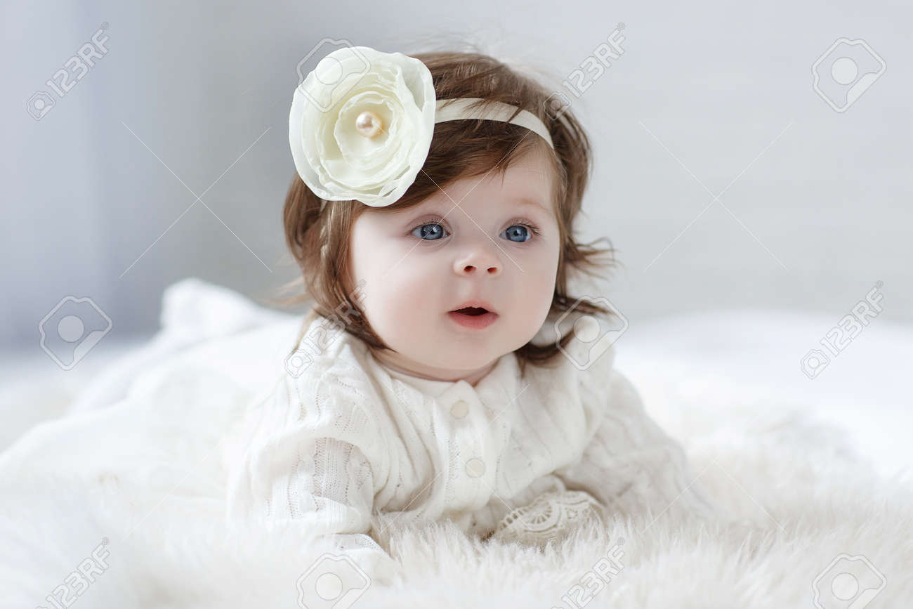Close-up Of A Six, Seven Months Old Baby Girl With Blue Eyes. Newborn Child,  Little Adorable Smiling And Attentive Girl Looking Surprised At The Camera.  Family, New Life, Childhood Concept. Christmas Eve