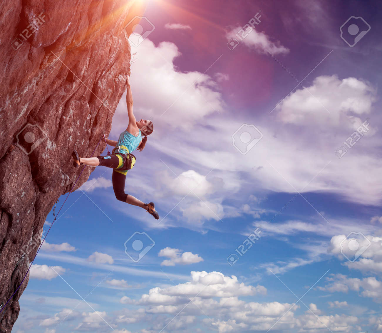 Elegant female athlete hanging at top of dangerous peak equipped with gear rope harness blue sky terrific clouds on background and sunbeams shining from above - 47706203 Elegant female athlete hanging at top of dangerous peak equipped with gear rope harness blue sky terrific clouds on background and sunbeams shining from above - 47706203