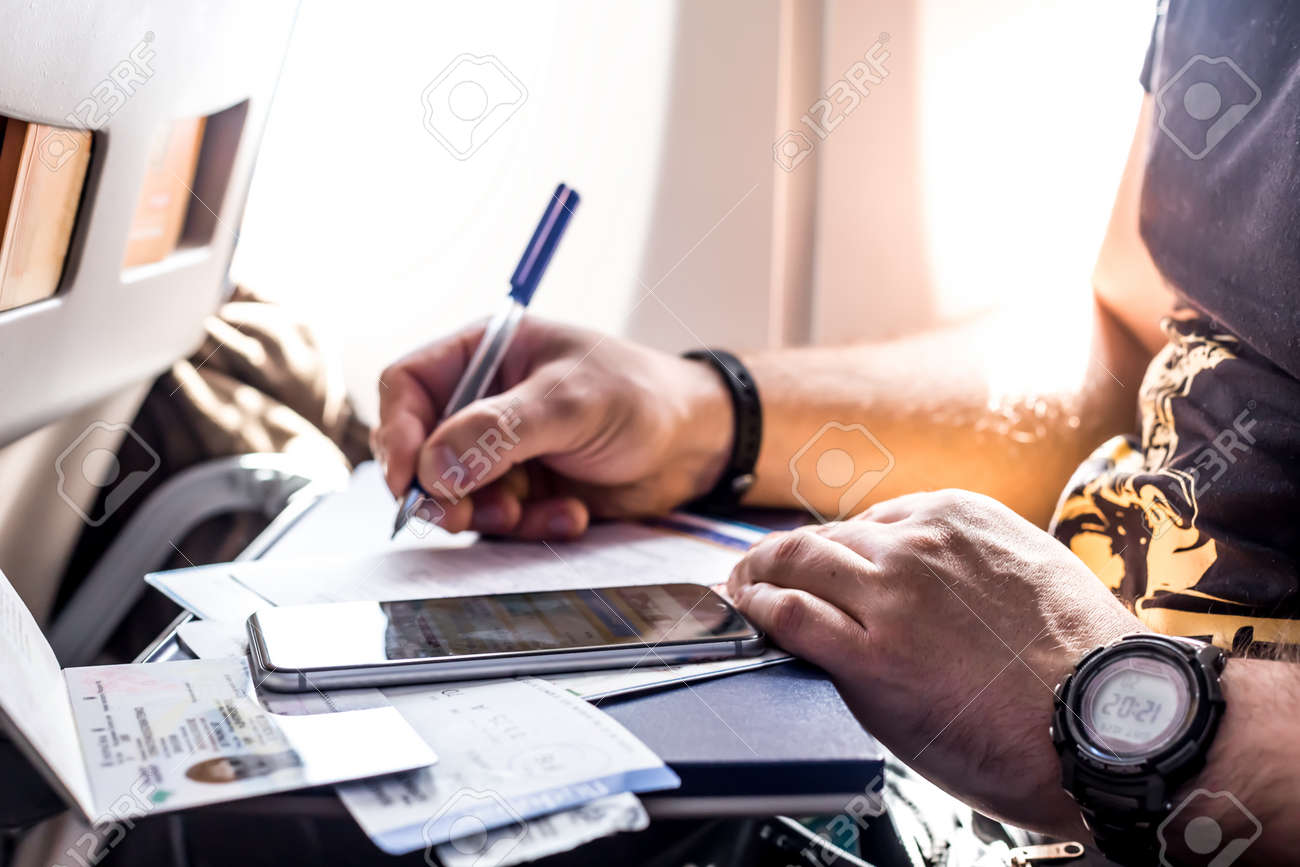 Man filling in immigration form sitting at airplane - 74074506 Man filling in immigration form sitting at airplane - 74074506