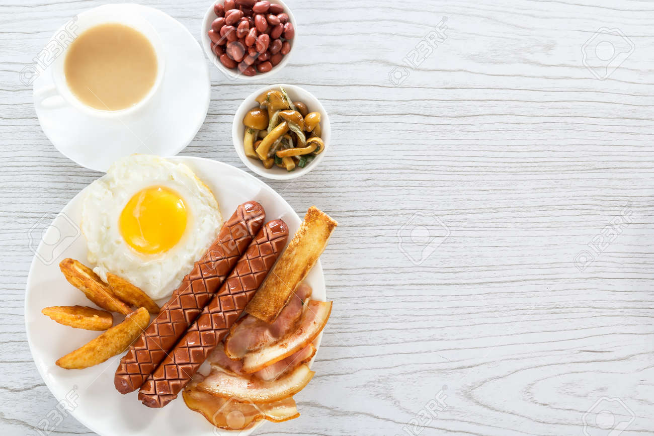 English Breakfast With Smoked Sausages Scrambled Eggs Bacon Mushrooms Toast And Beans Tea With Milk Breakfast On White Plate On A Light Background Space For Text View From Above Stock Photo Picture