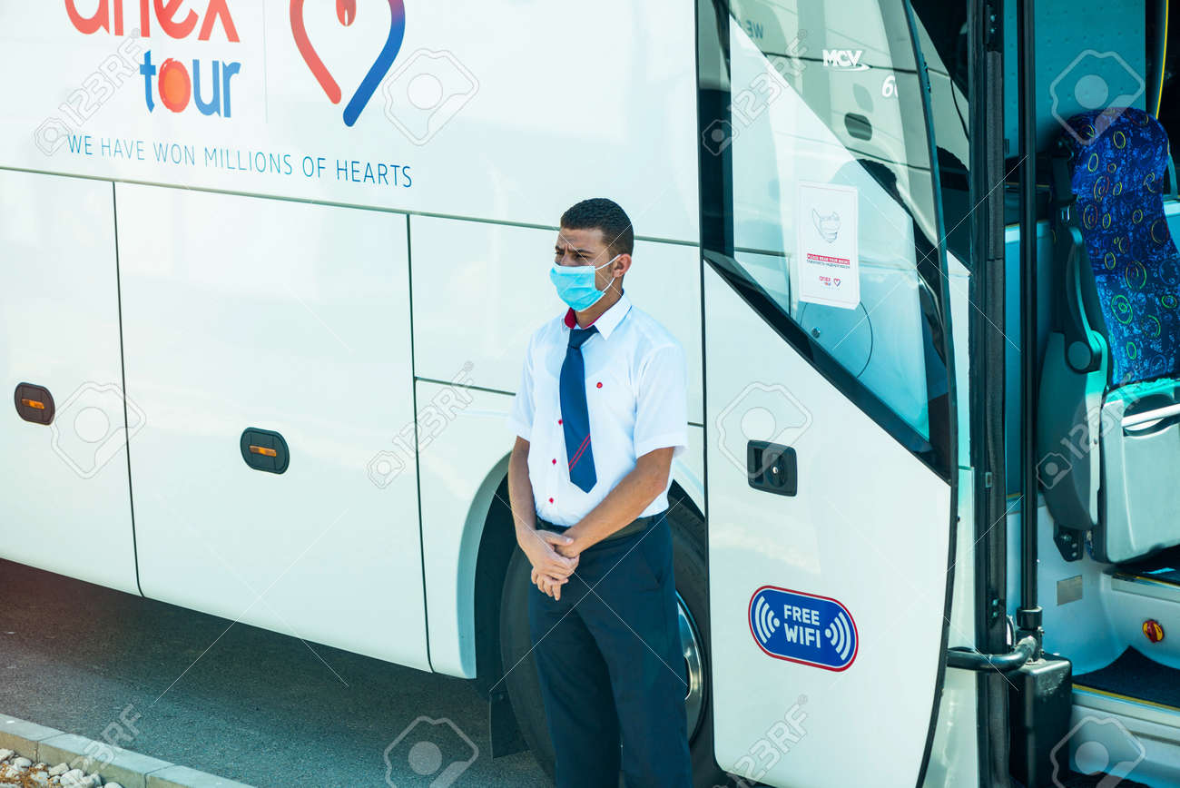 Egypt, Hurghada - 07/11/2020. tour guide in protective mask standing near buss entrance waiting for tourists - 154118504 Egypt, Hurghada - 07/11/2020. tour guide in protective mask standing near buss entrance waiting for tourists - 154118504