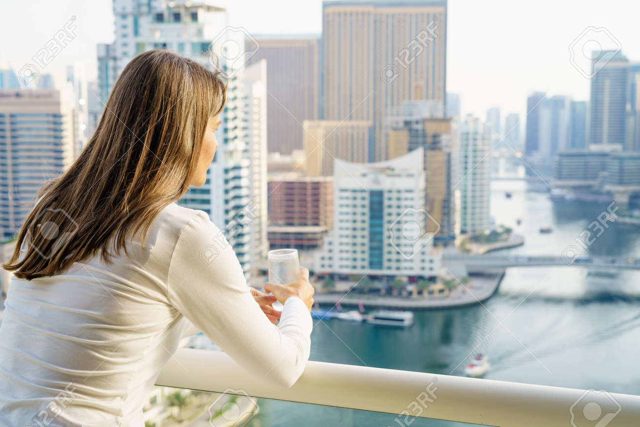 熟女は 高層ビルに彼女のバルコニーから街の景色を楽しんでいます の写真素材 画像素材 Image