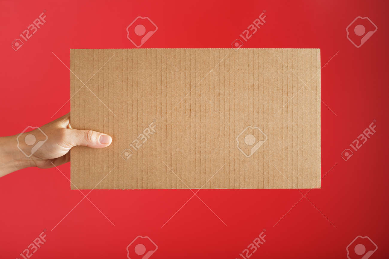Hand holding a blank sheet of cardboard on a red background. Space for text - 169206344 Hand holding a blank sheet of cardboard on a red background. Space for text - 169206344