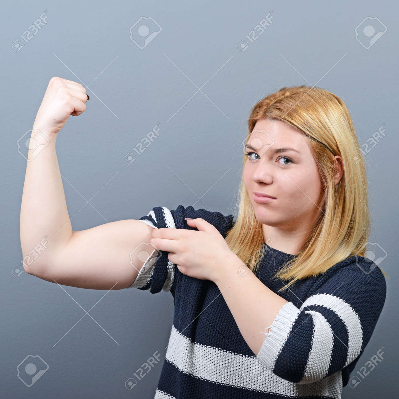 灰色の背景の彼女の腕に力こぶを見せてかなり若いブルネットの女性 の写真素材 画像素材 Image
