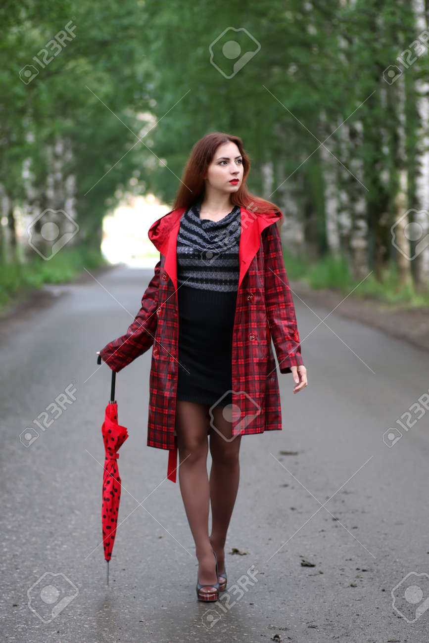 Beautiful Girl In A Red Raincoat With An Umbrella Walks In The