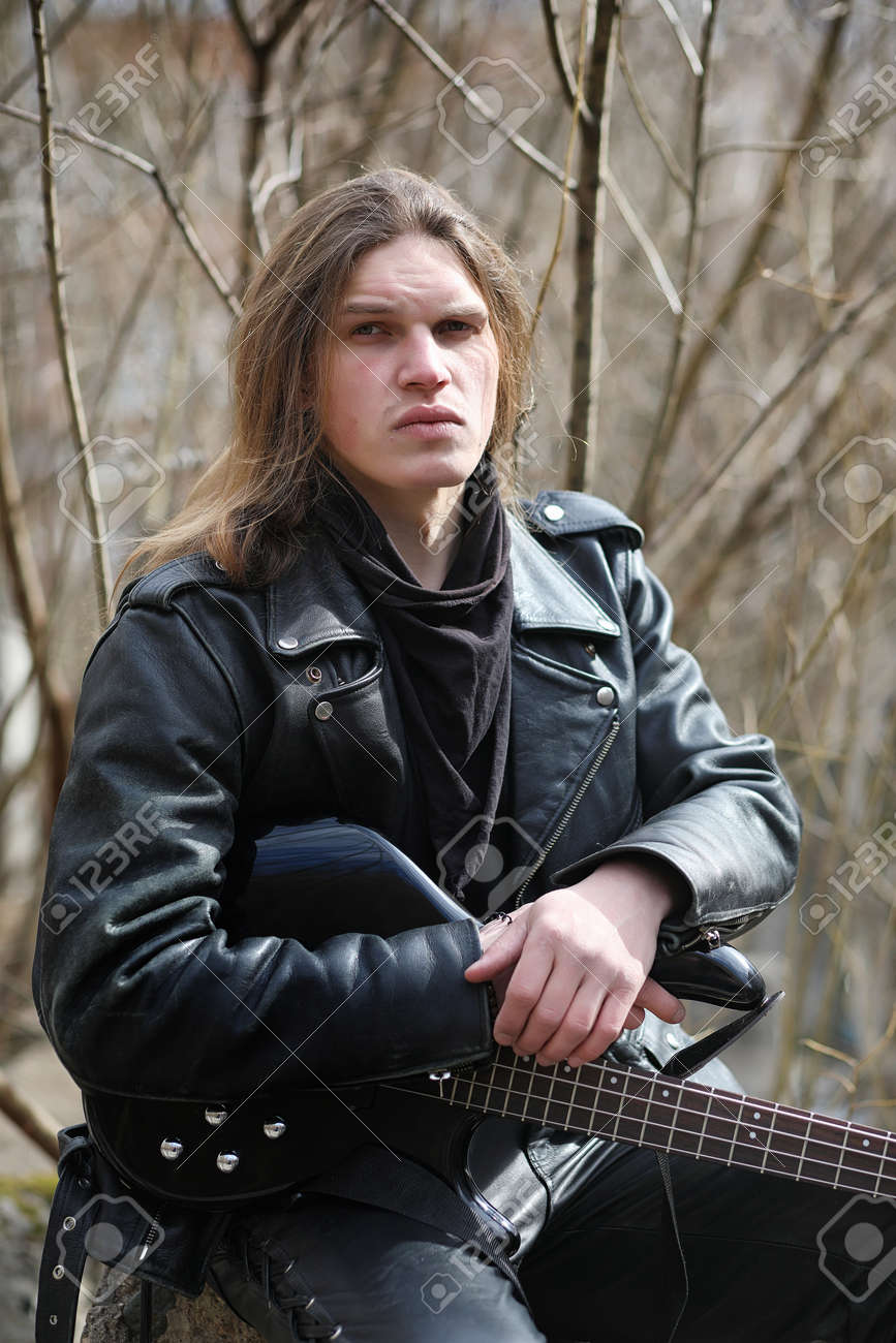 Un Músico En La Chaqueta Cuero Y Pantalones Sosteniendo Una Guitarra Baja Sentado Frente A Los En Un Parque Fotos, Retratos, Imágenes Y Fotografía De Archivo Libres De Derecho. Image
