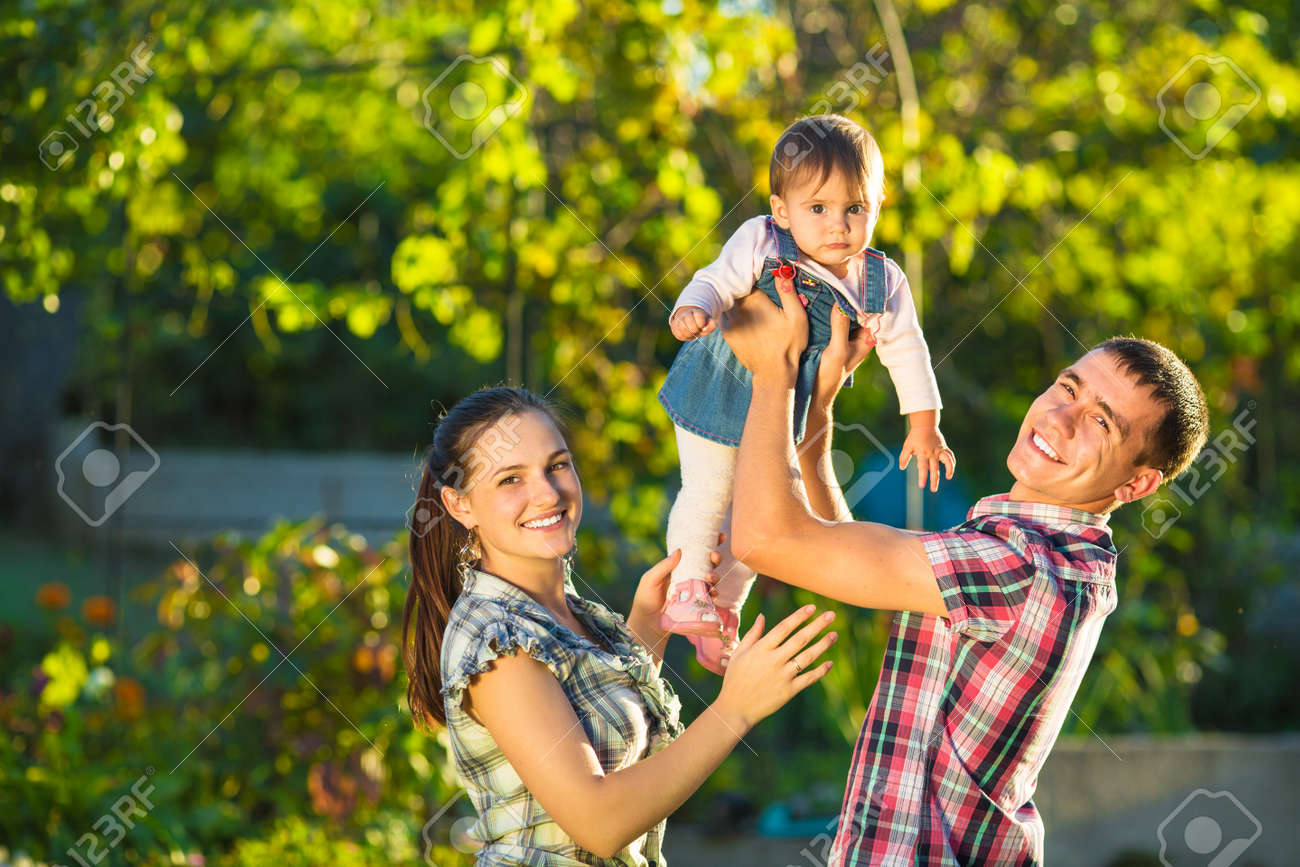 夏に屋外に楽しんで幸せな若い家族 母 父と自分のかわいい赤ちゃんは 日当たりの良い庭で遊んでいます 幸せの親と子供の頃のコンセプトです の写真素材 画像素材 Image