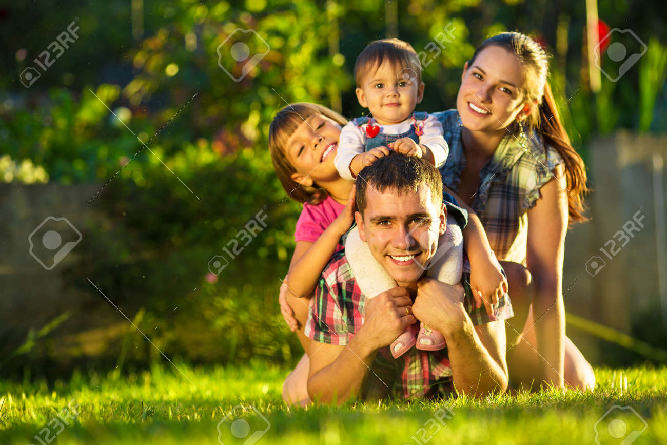 Happy young family having fun outdoors in summer. Mother, father and their cute little daughters are playing in the sunny garden. Happy parenthood and childhood concept. Focus on the father. - 32330509 Happy young family having fun outdoors in summer. Mother, father and their cute little daughters are playing in the sunny garden. Happy parenthood and childhood concept. Focus on the father. - 32330509