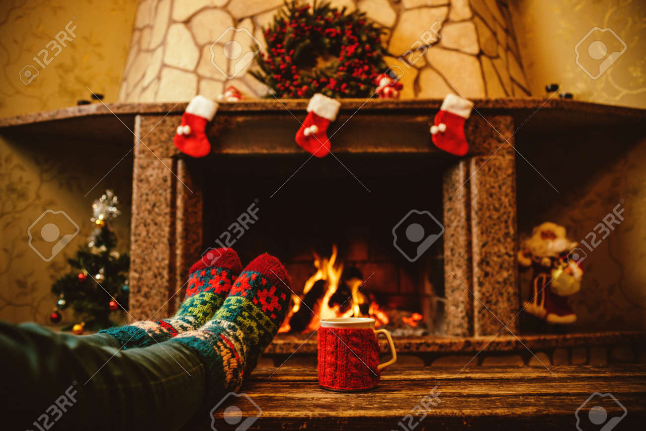 Feet in woollen socks by the Christmas fireplace. Woman relaxes by warm fire with a cup of hot drink and warming up her feet in woollen socks. Close up on feet. Winter and Christmas holidays concept. - 46927052 Feet in woollen socks by the Christmas fireplace. Woman relaxes by warm fire with a cup of hot drink and warming up her feet in woollen socks. Close up on feet. Winter and Christmas holidays concept. - 46927052