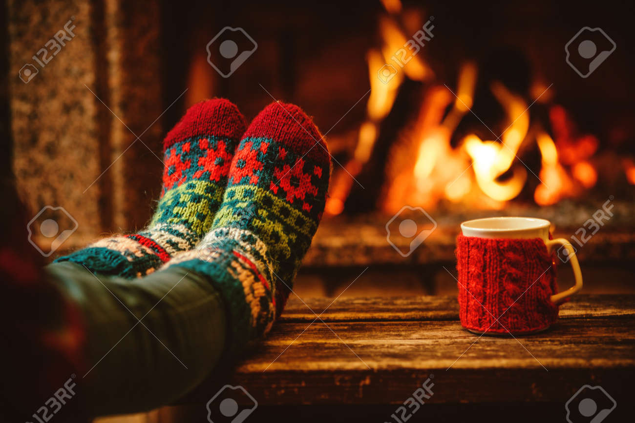 Feet in woollen socks by the Christmas fireplace. Woman relaxes by warm fire with a cup of hot drink and warming up her feet in woollen socks. Close up on feet. Winter and Christmas holidays concept. - 46927059 Feet in woollen socks by the Christmas fireplace. Woman relaxes by warm fire with a cup of hot drink and warming up her feet in woollen socks. Close up on feet. Winter and Christmas holidays concept. - 46927059