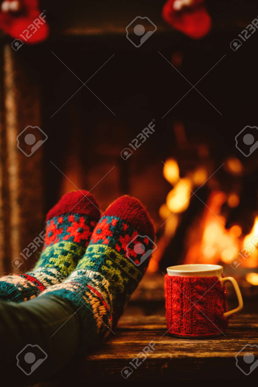Feet in woollen socks by the Christmas fireplace. Woman relaxes by warm fire with a cup of hot drink and warming up her feet in woollen socks. Close up on feet. Winter and Christmas holidays concept. - 46927060 Feet in woollen socks by the Christmas fireplace. Woman relaxes by warm fire with a cup of hot drink and warming up her feet in woollen socks. Close up on feet. Winter and Christmas holidays concept. - 46927060