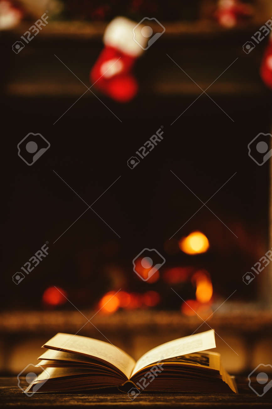 Open book by the Fireplace with Christmas ornaments. Open storybook lying on a wooden bench by the fireside. Cozy relaxed magical atmosphere in a chalet house decorated for Christmas. Holiday concept. - 46927125 Open book by the Fireplace with Christmas ornaments. Open storybook lying on a wooden bench by the fireside. Cozy relaxed magical atmosphere in a chalet house decorated for Christmas. Holiday concept. - 46927125