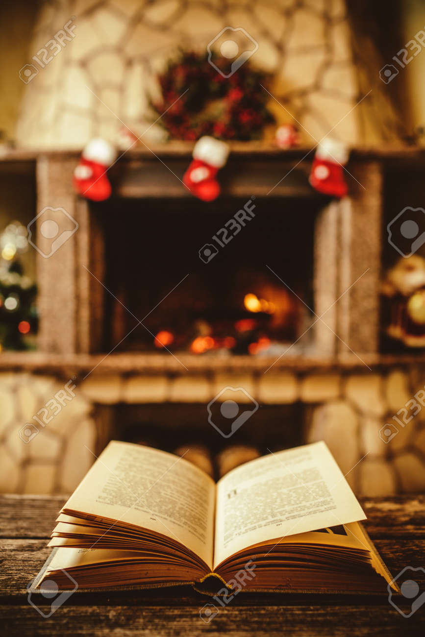 Open book by the Fireplace with Christmas ornaments. Open storybook lying on a wooden bench by the fireside. Cozy relaxed magical atmosphere in a chalet house decorated for Christmas. Holiday concept. - 46927127 Open book by the Fireplace with Christmas ornaments. Open storybook lying on a wooden bench by the fireside. Cozy relaxed magical atmosphere in a chalet house decorated for Christmas. Holiday concept. - 46927127