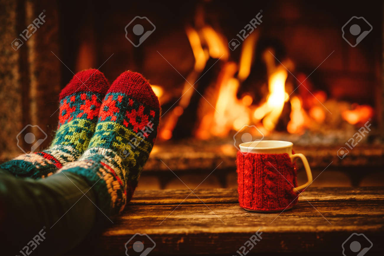 Feet in woollen socks by the Christmas fireplace. Woman relaxes by warm fire with a cup of hot drink and warming up her feet in woollen socks. Close up on feet. Winter and Christmas holidays concept. - 46927175 Feet in woollen socks by the Christmas fireplace. Woman relaxes by warm fire with a cup of hot drink and warming up her feet in woollen socks. Close up on feet. Winter and Christmas holidays concept. - 46927175