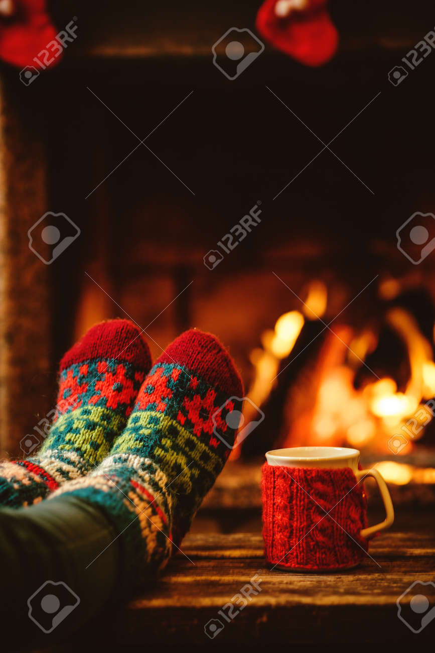 Feet in woollen socks by the Christmas fireplace. Woman relaxes by warm fire with a cup of hot drink and warming up her feet in woollen socks. Close up on feet. Winter and Christmas holidays concept. - 46927176 Feet in woollen socks by the Christmas fireplace. Woman relaxes by warm fire with a cup of hot drink and warming up her feet in woollen socks. Close up on feet. Winter and Christmas holidays concept. - 46927176