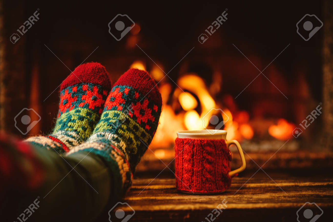 Feet in woollen socks by the Christmas fireplace. Woman relaxes by warm fire with a cup of hot drink and warming up her feet in woollen socks. Close up on feet. Winter and Christmas holidays concept. - 46927179 Feet in woollen socks by the Christmas fireplace. Woman relaxes by warm fire with a cup of hot drink and warming up her feet in woollen socks. Close up on feet. Winter and Christmas holidays concept. - 46927179