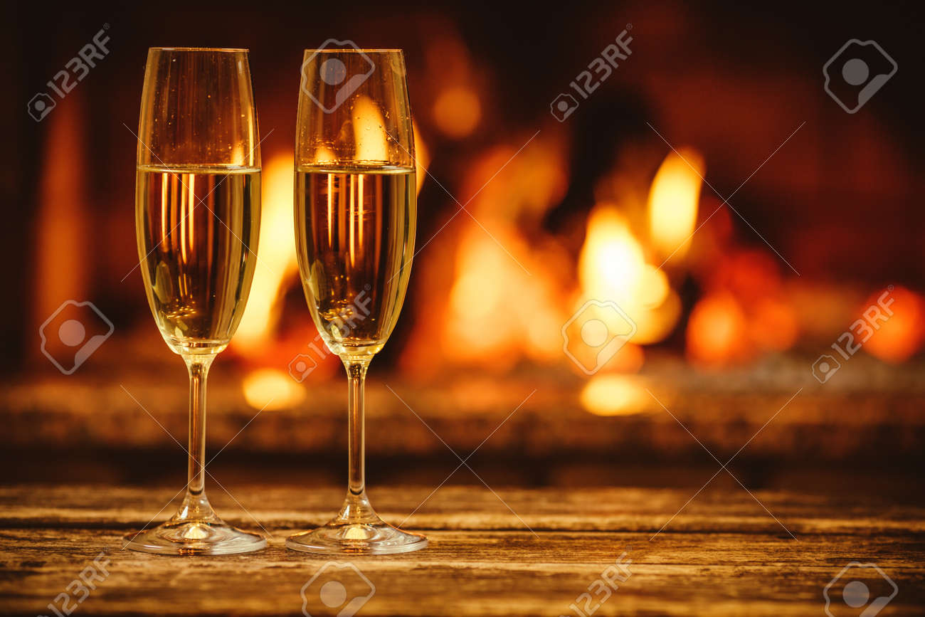 Two glasses of sparkling champagne in front of warm fireplace. Cozy relaxed magical atmosphere in a chalet house by the fireside. Snug holiday concept. Beautiful background with shimmering wine. - 46927181 Two glasses of sparkling champagne in front of warm fireplace. Cozy relaxed magical atmosphere in a chalet house by the fireside. Snug holiday concept. Beautiful background with shimmering wine. - 46927181