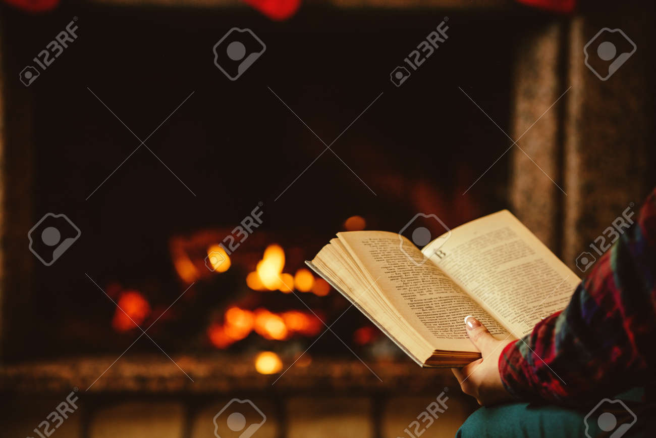 Woman reading a book by the fireplace. Young woman reading a book by the warm fireplace decorated for Christmas. Relaxed holiday evening concept. - 46927144 Woman reading a book by the fireplace. Young woman reading a book by the warm fireplace decorated for Christmas. Relaxed holiday evening concept. - 46927144