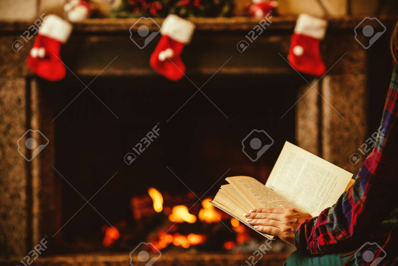 Woman reading a book by the fireplace. Young woman reading a book by the warm fireplace decorated for Christmas. Relaxed holiday evening concept. - 46927063 Woman reading a book by the fireplace. Young woman reading a book by the warm fireplace decorated for Christmas. Relaxed holiday evening concept. - 46927063