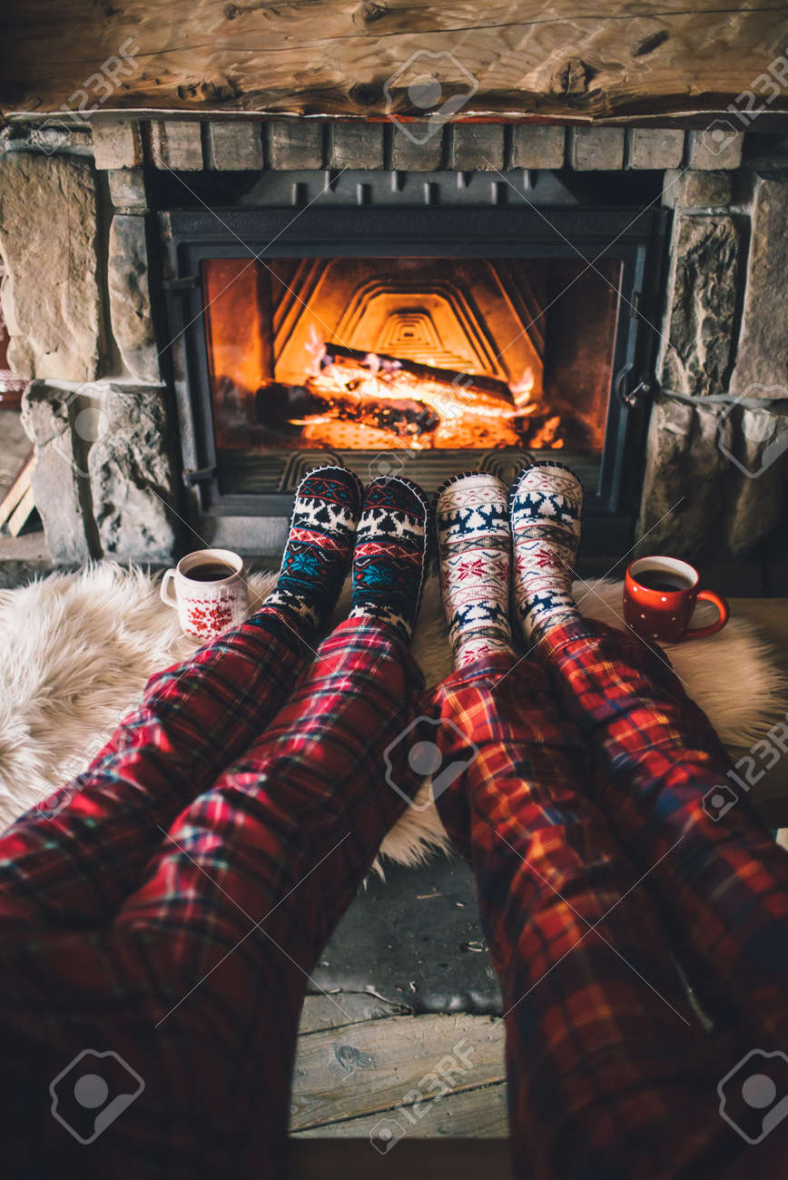 Couple sitting under the blanket, relaxes by warm fire and warming up their feet in woolen socks. - 58947458 Couple sitting under the blanket, relaxes by warm fire and warming up their feet in woolen socks. - 58947458