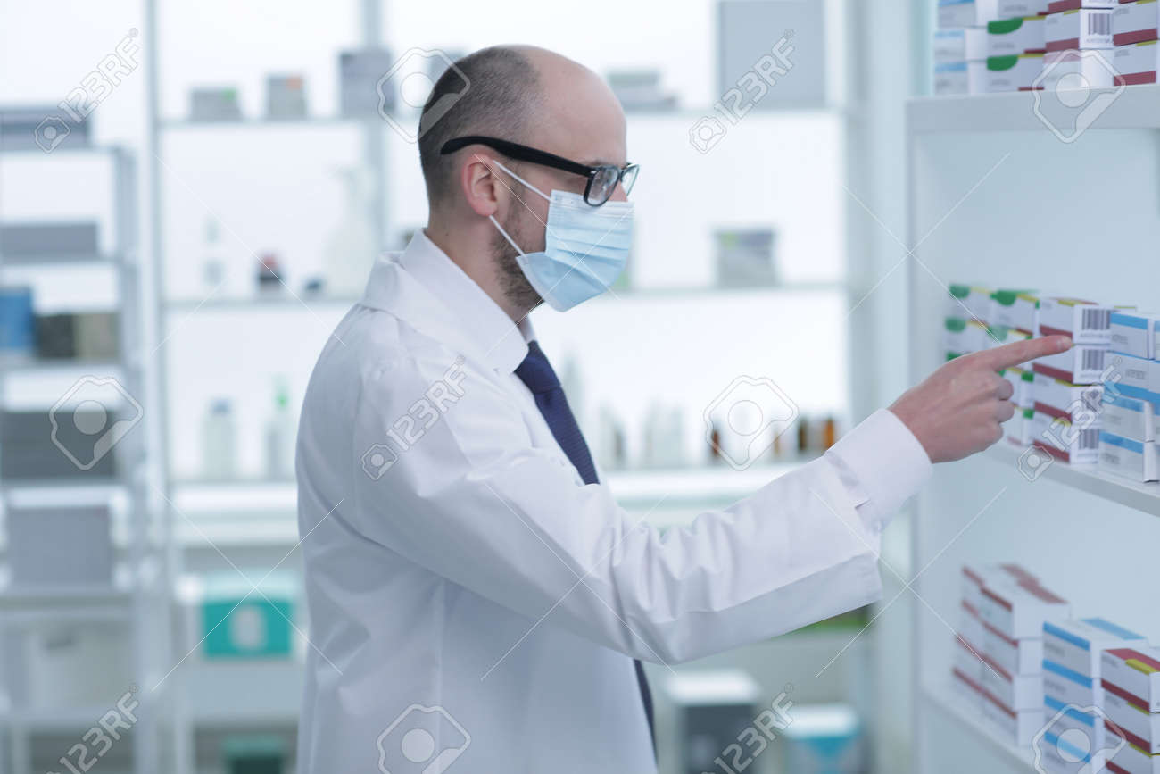 Man pharmacist in protective face mask working in drugstore - 168862485 Man pharmacist in protective face mask working in drugstore - 168862485