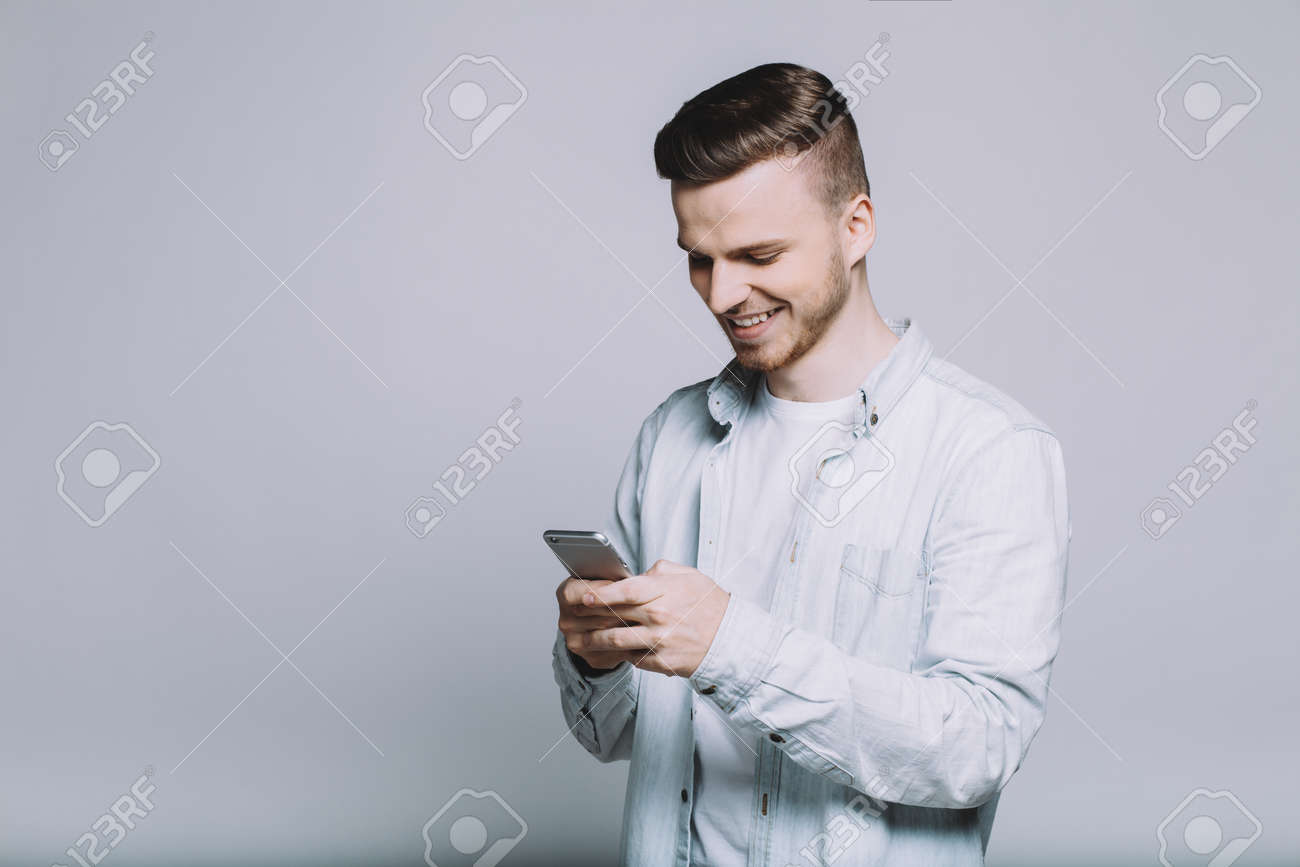 Young Stylish Smiling Guy Is Watching Funny Video On His Mobile Phone. He Is Happy Because He Has Seen Something Interesting. Profile View. Close Up. Isolated Stock Photo, Picture And Royalty Free Young Stylish Smiling Guy Is Watching Funny Video On His Mobile Phone. He Is Happy Because He Has Seen Something Interesting. Profile View. Close Up. Isolated Stock Photo, Picture And Royalty Free