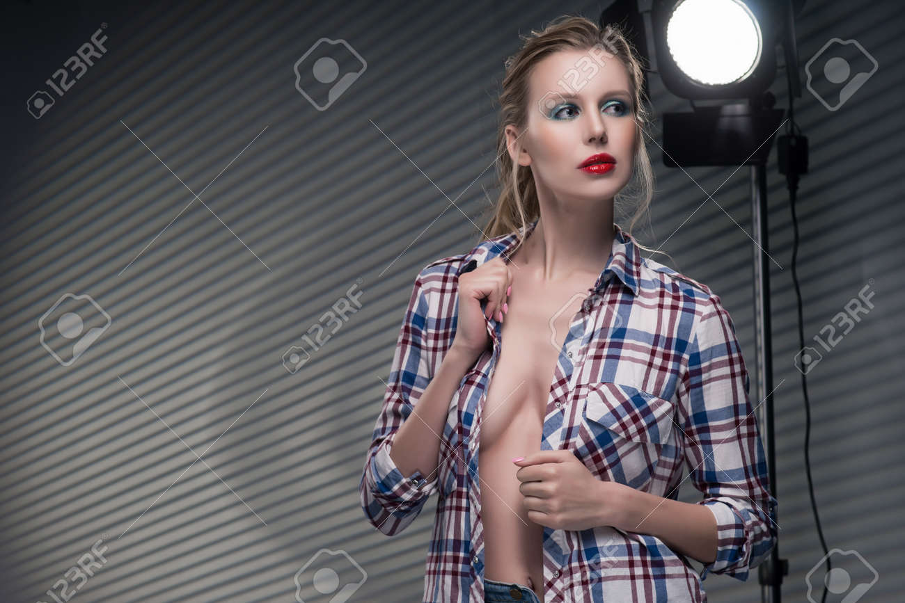 slender big tits Beautiful Slender Blonde Big Breast Girl Without A Bra Wearing Unbuttoned Checkered Shirt And Jeans On A Striped Gray Background Near The Studio Lamp. Copy Space. Advertising, Fashion, And Commercial Stock Photo,