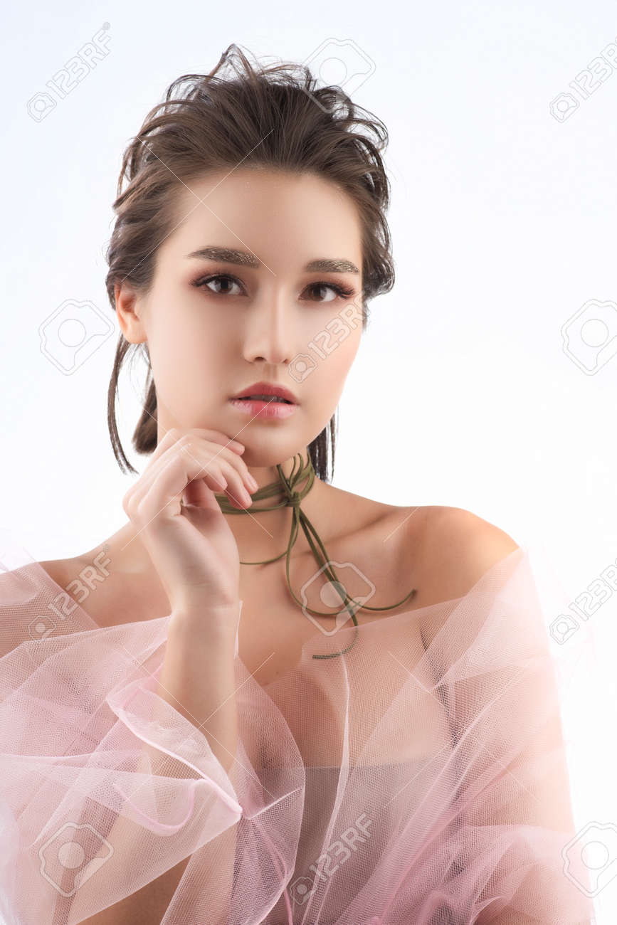 Beautiful young big breast asian girl wearing a pink veil on her naked  shoulders and a choker on her neck sensually touches her face and neck.  Isolated on white. Smooth healthy skin.