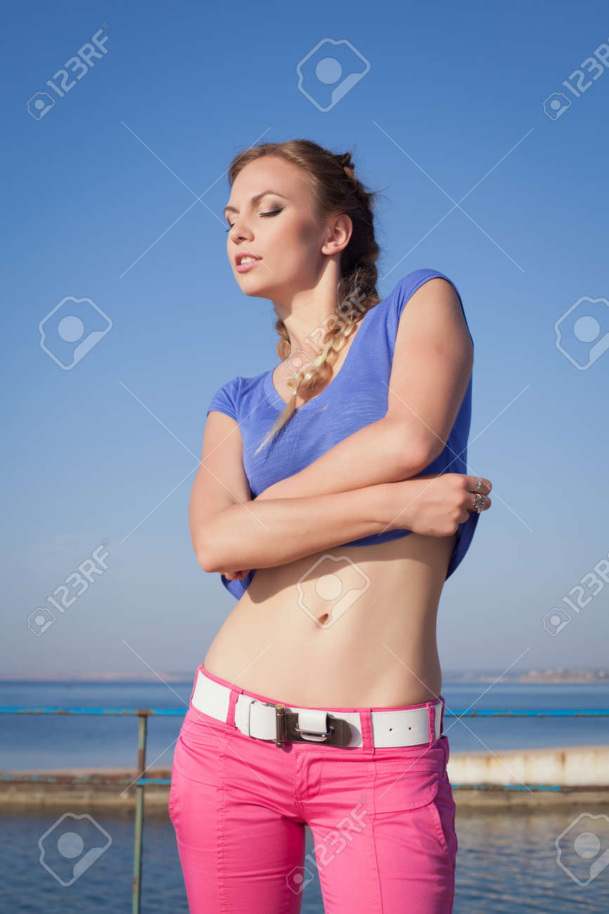 オープンエアのおさげ髪の少女 ピンクのズボンの若い女性が海に彼のシャツを脱ぐ の写真素材 画像素材 Image